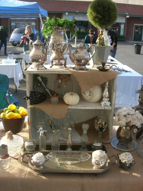 A display of vintage silverware, decorative items, and a small pumpkin on a rustic shelf at an outdoor market.