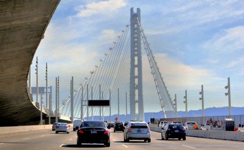 A view of a cable-stayed bridge with cars driving on a highway beneath a clear blue sky.