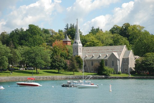 A serene waterfront scene featuring a church with a steeple, surrounded by trees and boats on the water.