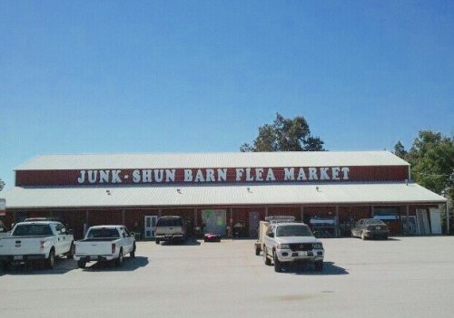 A red barn-style building with "Junk Shun Barn Flea Market" sign, surrounded by parked trucks under a clear blue sky.