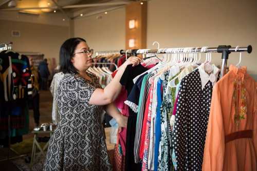 A woman browses a rack of colorful dresses in a well-lit room filled with clothing.