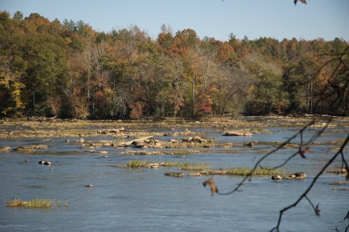 A serene river scene with rocky outcrops and autumn foliage along the banks under a clear blue sky.