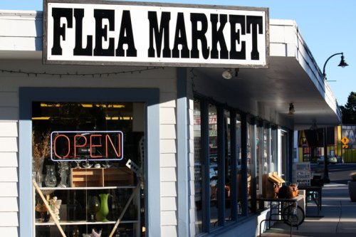 A storefront with a "Flea Market" sign and an "Open" neon sign, showcasing various items inside.
