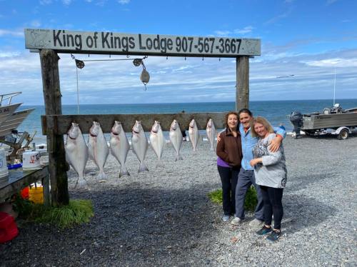 Three people pose in front of a sign at King of Kings Lodge, with several fish displayed on a rack nearby.