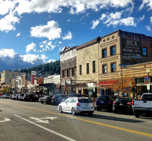 A charming street lined with historic buildings, shops, and parked cars under a blue sky with fluffy clouds.