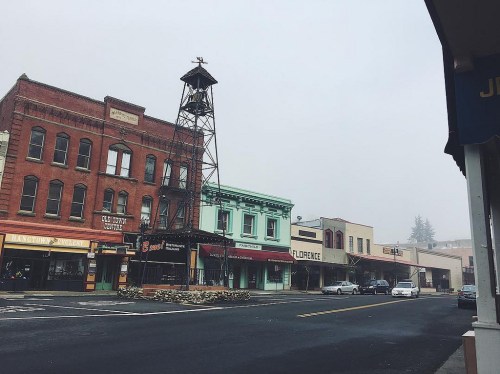 Foggy street scene featuring historic buildings, a clock tower, and empty sidewalks in a small town.