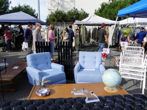 A flea market scene with blue chairs, a globe, and various vendors selling clothing and furniture in the background.