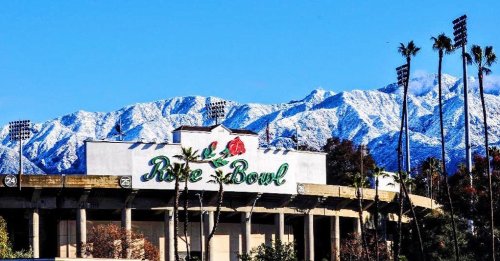 The Rose Bowl stadium with snow-capped mountains in the background and palm trees in the foreground.