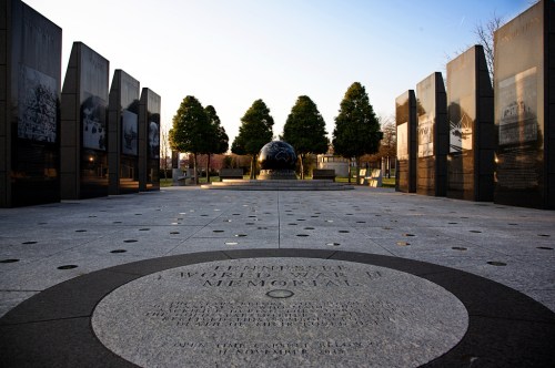 A memorial site featuring stone panels, trees, and a globe, set against a clear sky.
