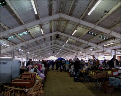 A bustling indoor market with vendors and shoppers, featuring various stalls and a high, arched ceiling.