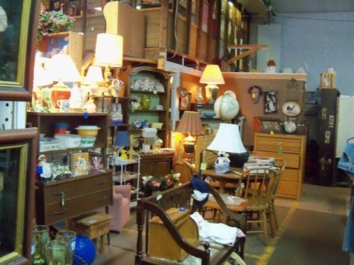 A cozy antique shop filled with vintage furniture, lamps, and decorative items on shelves and tables.