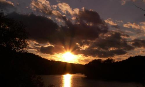 Sunset over a calm lake, with vibrant clouds and rays of sunlight reflecting on the water's surface.