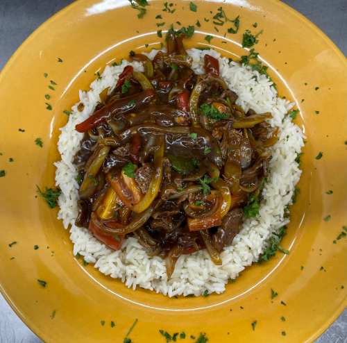 A plate of white rice topped with a savory beef and vegetable stir-fry, garnished with fresh herbs.