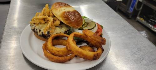 A juicy burger topped with cheese and crispy onions, served with lettuce, tomato, pickles, and a side of onion rings.