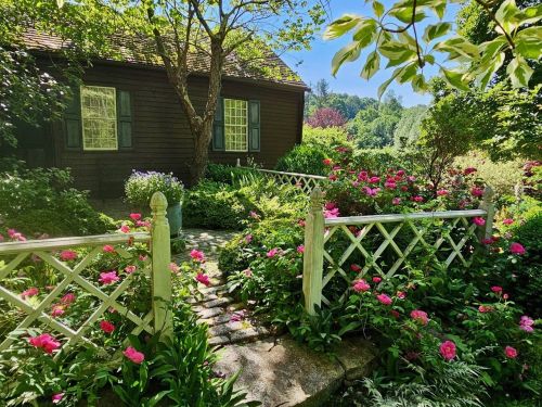 A charming garden with vibrant flowers and a quaint wooden house surrounded by lush greenery and a white picket fence.