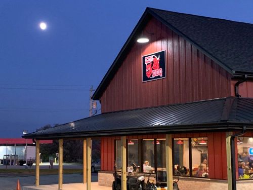 A red barn-style restaurant with a BBQ sign, illuminated at dusk, with a full moon in the sky above.