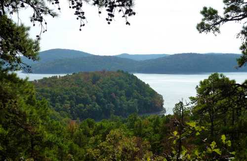 A serene view of a lake surrounded by lush green hills and trees under a clear sky.