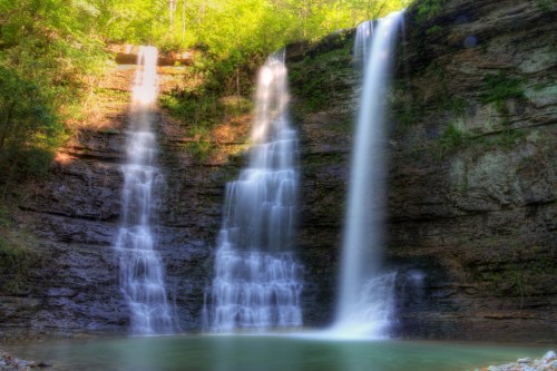 A serene waterfall cascading down rocky cliffs into a tranquil pool, surrounded by lush green foliage.