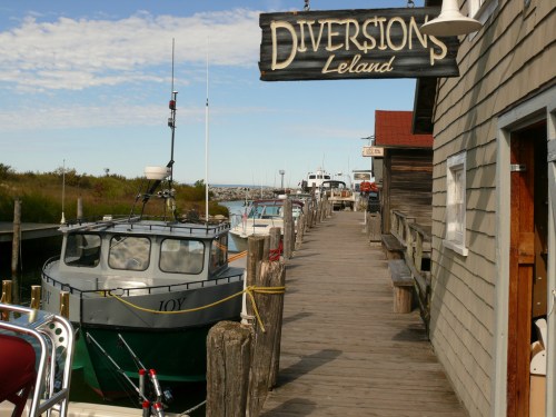 A wooden dock lined with boats, featuring a sign that reads "Diversions Leland" against a clear blue sky.