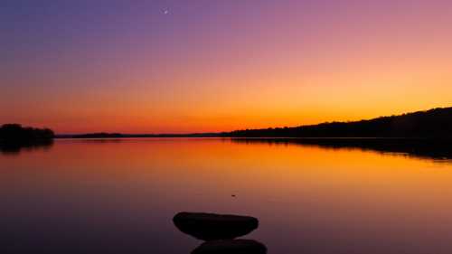 A serene sunset over a calm lake, with vibrant orange and purple hues reflecting on the water's surface.