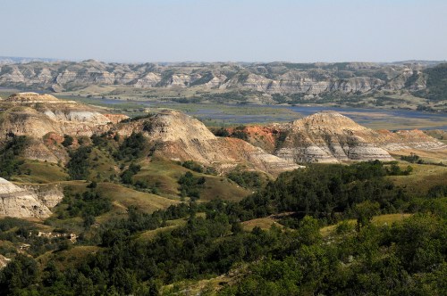 A panoramic view of rolling hills and layered rock formations, with a river winding through a lush valley in the background.