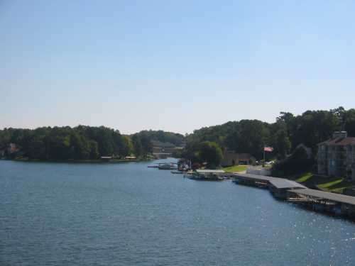 A serene lake view with boats, docks, and lush greenery under a clear blue sky.