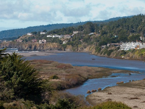 A scenic view of a river winding through a coastal landscape with homes on the hillside and lush greenery.