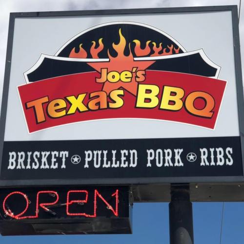 Sign for Joe's Texas BBQ featuring flames, with "Brisket, Pulled Pork, Ribs" and an "OPEN" neon sign.