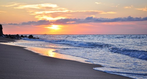 A serene beach at sunset, with gentle waves lapping at the shore and colorful clouds in the sky.