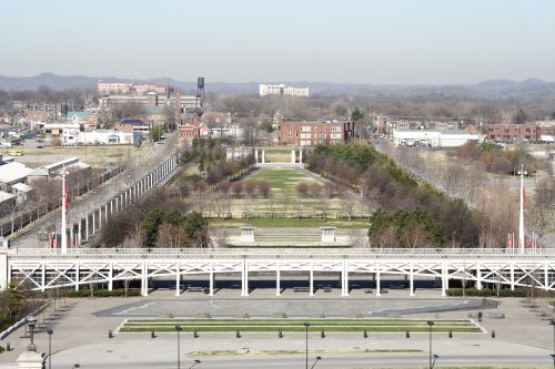 Aerial view of a park with pathways, trees, and buildings in the background on a clear day.