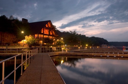 A serene lakeside scene at dusk, featuring a lodge and illuminated docks reflecting on the water.