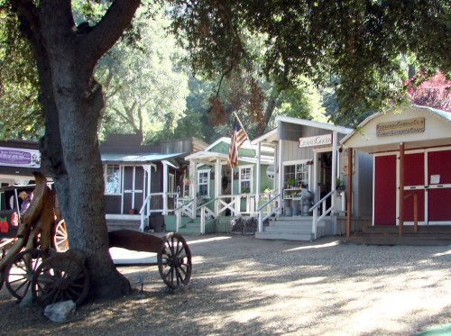 Quaint buildings with porches and an American flag, surrounded by trees and gravel, evoking a charming small-town atmosphere.