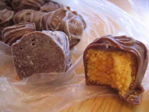 Close-up of chocolate candies, one partially bitten to reveal a soft, orange filling inside.