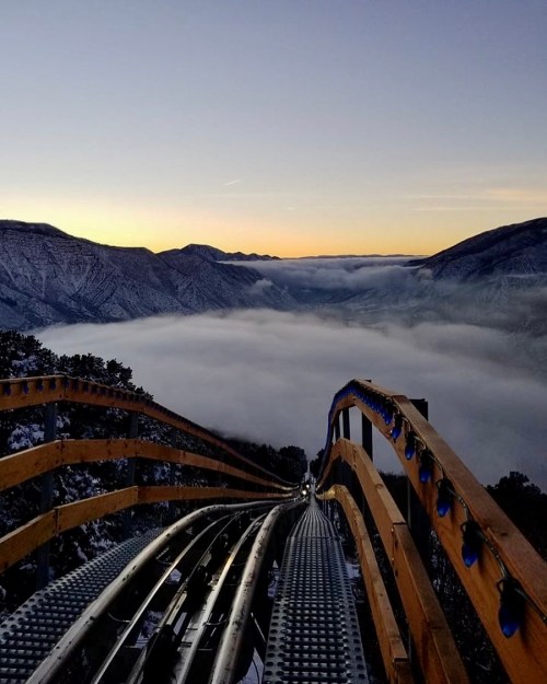 A scenic view from a roller coaster track overlooking mountains and fog at sunrise.