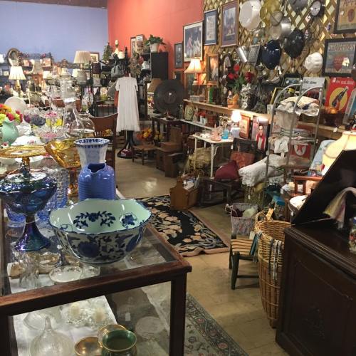 A cozy antique shop filled with various vintage items, including glassware, furniture, and decorative pieces.