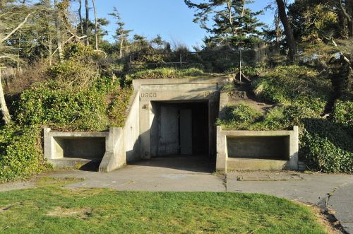 Concrete entrance to a bunker surrounded by greenery, with benches on either side and trees in the background.