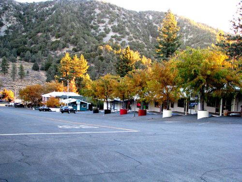 A quiet street lined with trees and small buildings, set against a backdrop of mountains in autumn.