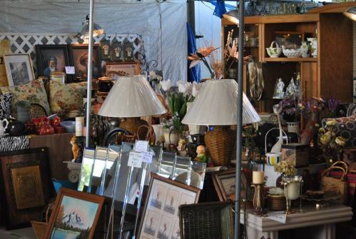 A bustling antique market display featuring lamps, mirrors, and various vintage items on tables and shelves.
