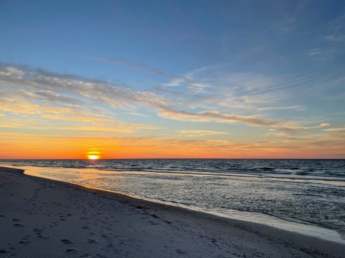 A serene beach at sunset, with gentle waves and a colorful sky filled with clouds.