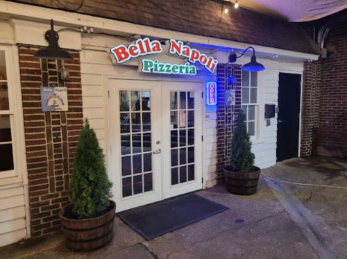 Exterior of Bella Napoli Pizzeria, featuring a welcoming entrance with an "Open" sign and decorative plants.