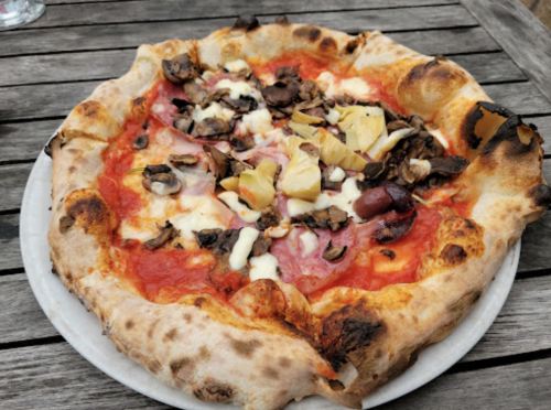 A freshly baked pizza topped with mushrooms, ham, cheese, and pineapple on a wooden table.