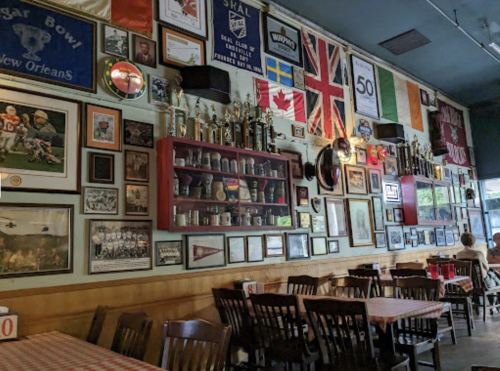 A cozy restaurant wall adorned with trophies, photos, and flags, featuring wooden tables and checkered tablecloths.