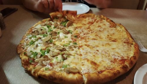 A large pizza divided into two halves: one with cheese and the other topped with mushrooms and green peppers.