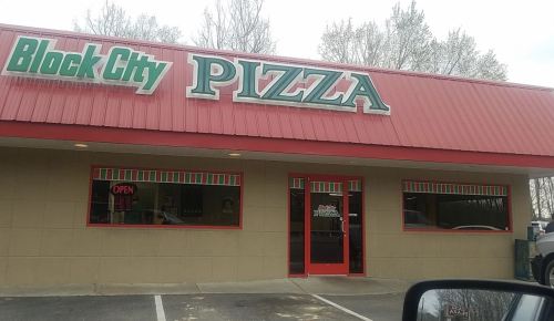 Exterior of Block City Pizza, featuring a red roof, green and white signage, and large windows with an "Open" sign.
