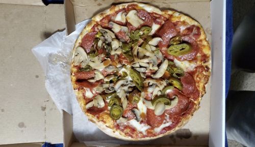A pizza topped with pepperoni, mushrooms, jalapeños, and green peppers in a pizza box.