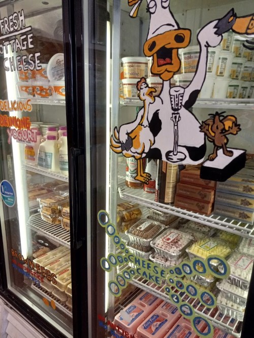 Refrigerator display filled with dairy products, featuring a cartoon cow and chickens on the glass door.