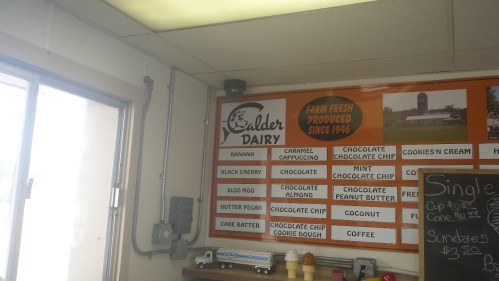 Menu board at Calder Dairy featuring various ice cream flavors and a farm image, with a bright, well-lit interior.