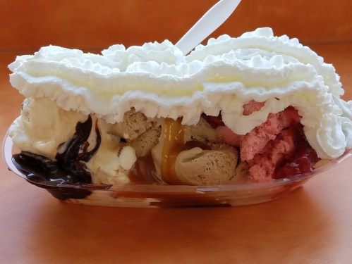 A colorful ice cream sundae with three flavors, topped with whipped cream and a drizzle of syrup.