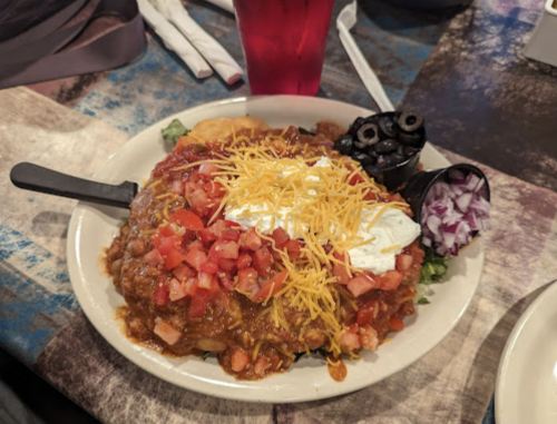 A colorful plate of nachos topped with chili, tomatoes, cheese, sour cream, olives, and onions on a bed of lettuce.