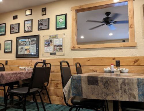 Interior of a restaurant featuring tables, chairs, wall decor, and a ceiling fan.